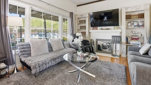 A living room with a sofa, a round glass coffee table, a fireplace, and a TV mounted on the wall.