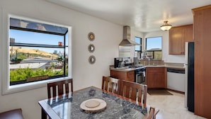 A modern kitchen with a dining area, large windows, and a view of the city.