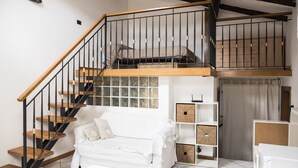 Un dormitorio tipo loft moderno con escalera de madera, sofá blanco y unidades de almacenaje integradas.