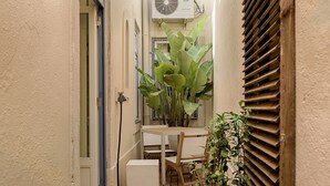 A narrow outdoor space with a wooden table and chairs, a potted plant, and a window with shutters. - Romantic Gem in Alfama (Lisboa)