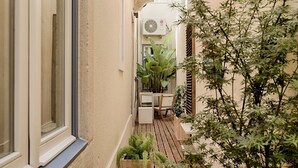 A narrow outdoor corridor with a wooden floor, a window on the left, and a small seating area with a table and chair. - Romantic Gem in Alfama (Lisboa)