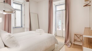 A bedroom with a bed, a wooden nightstand, a whiteboard, and a window with curtains. - Romantic Gem in Alfama (Lisboa)