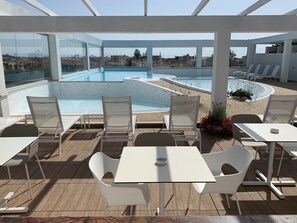 Un área de piscina en la azotea con sillas y mesas blancas, vistas despejadas del paisaje urbano y un diseño arquitectónico moderno.