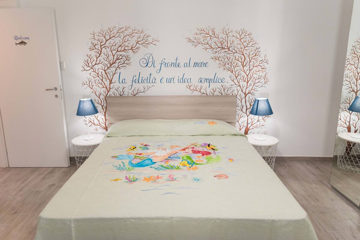 Una camera da letto con un letto, due comodini e un muro decorato con un affresco.