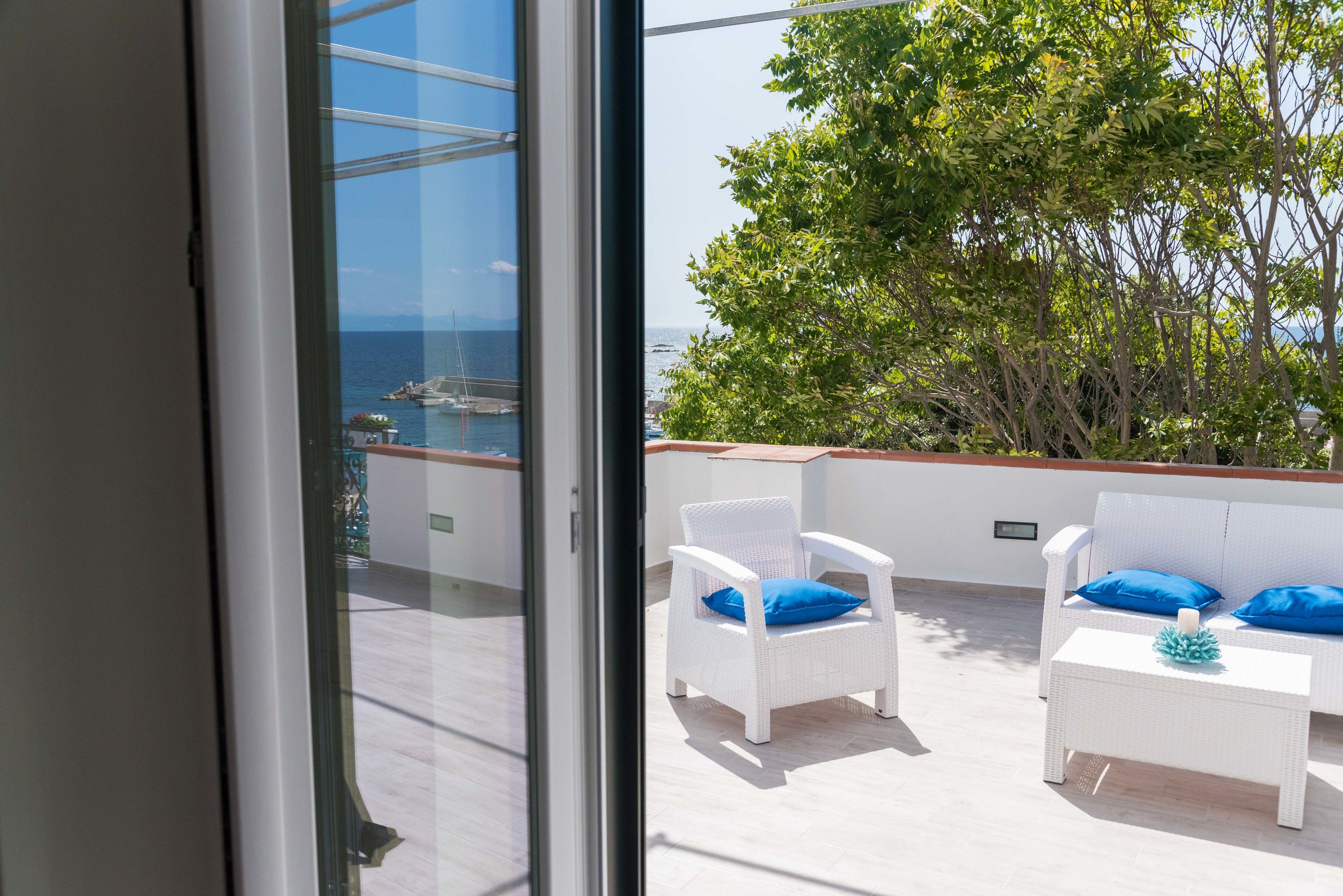 Een balkon met witte rieten meubels, uitzicht op zee en een boom.