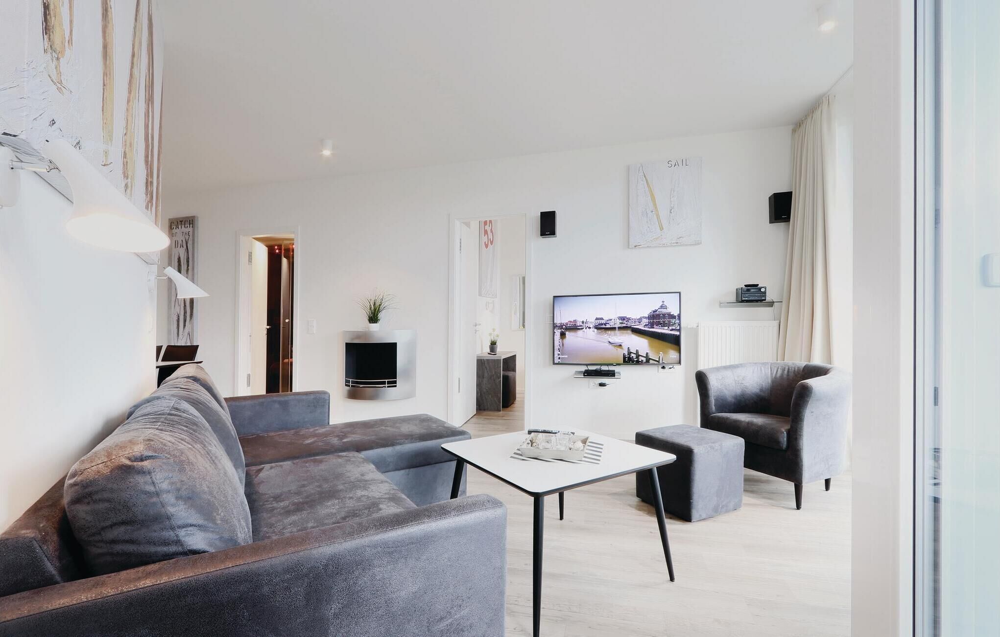 Ein modernes Wohnzimmer mit grauem Sofa, einem Couchtisch und einem Fernseher, der eine Stadtansicht zeigt.