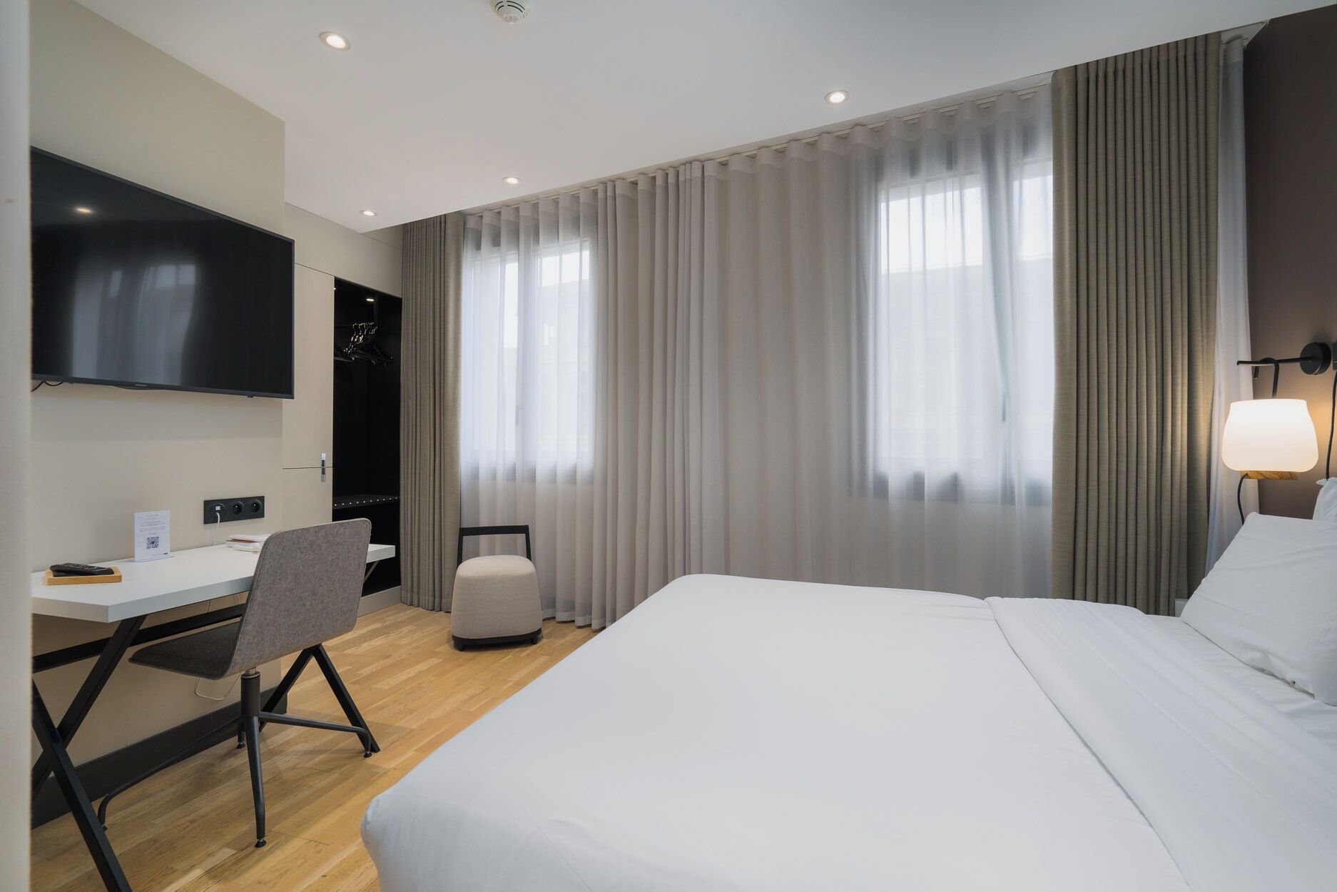 A hotel room with a bed, a desk, a chair, a TV, and a lamp.