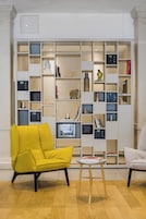Un interno moderno con una poltrona gialla, un piccolo tavolino rotondo e una libreria piena di oggetti assortiti.