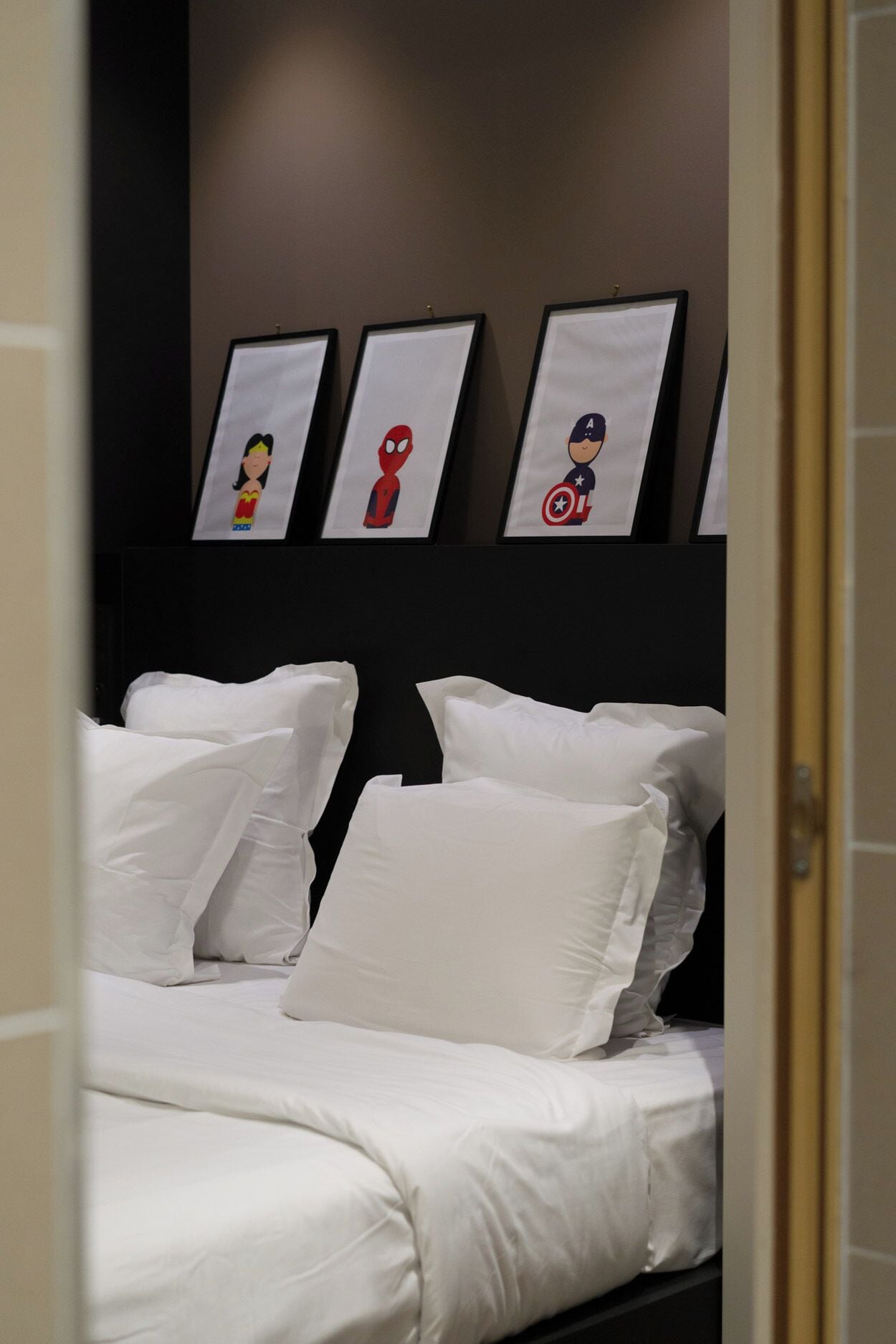 Una cama bien hecha con sábanas y almohadas blancas, cabecera oscura y tres cuadros enmarcados sobre la cama.
