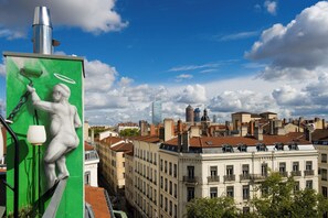 A cityscape with a statue of a figure on a green wall, buildings with varied architecture, and a clear sky.