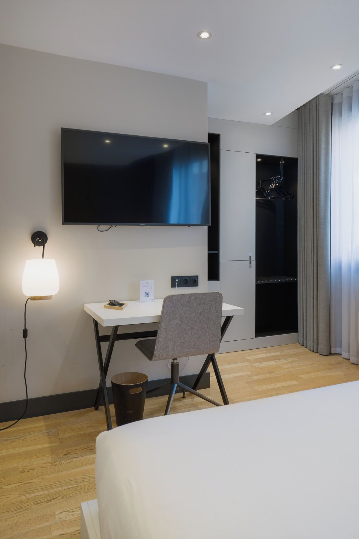Ett hotellrum med en platt-TV som är monterad på väggen, ett skrivbord med en stol, ett nattduksbord och en stor säng.