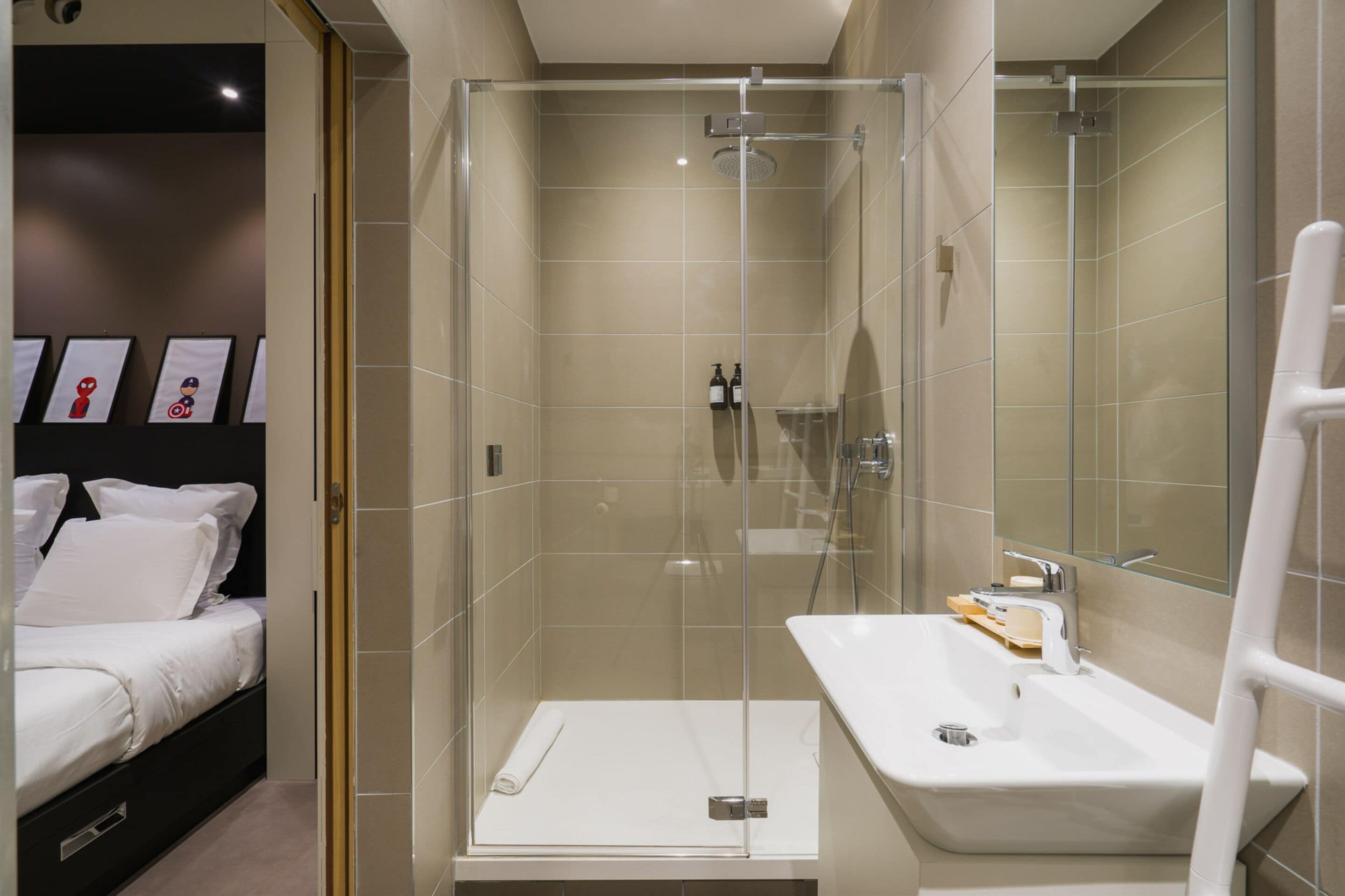 A modern bathroom with a glass-enclosed shower, a white sink, and a bed with white bedding.