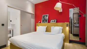 A modern bedroom with a large bed, a red accent wall, a bedside lamp, and a mirror.