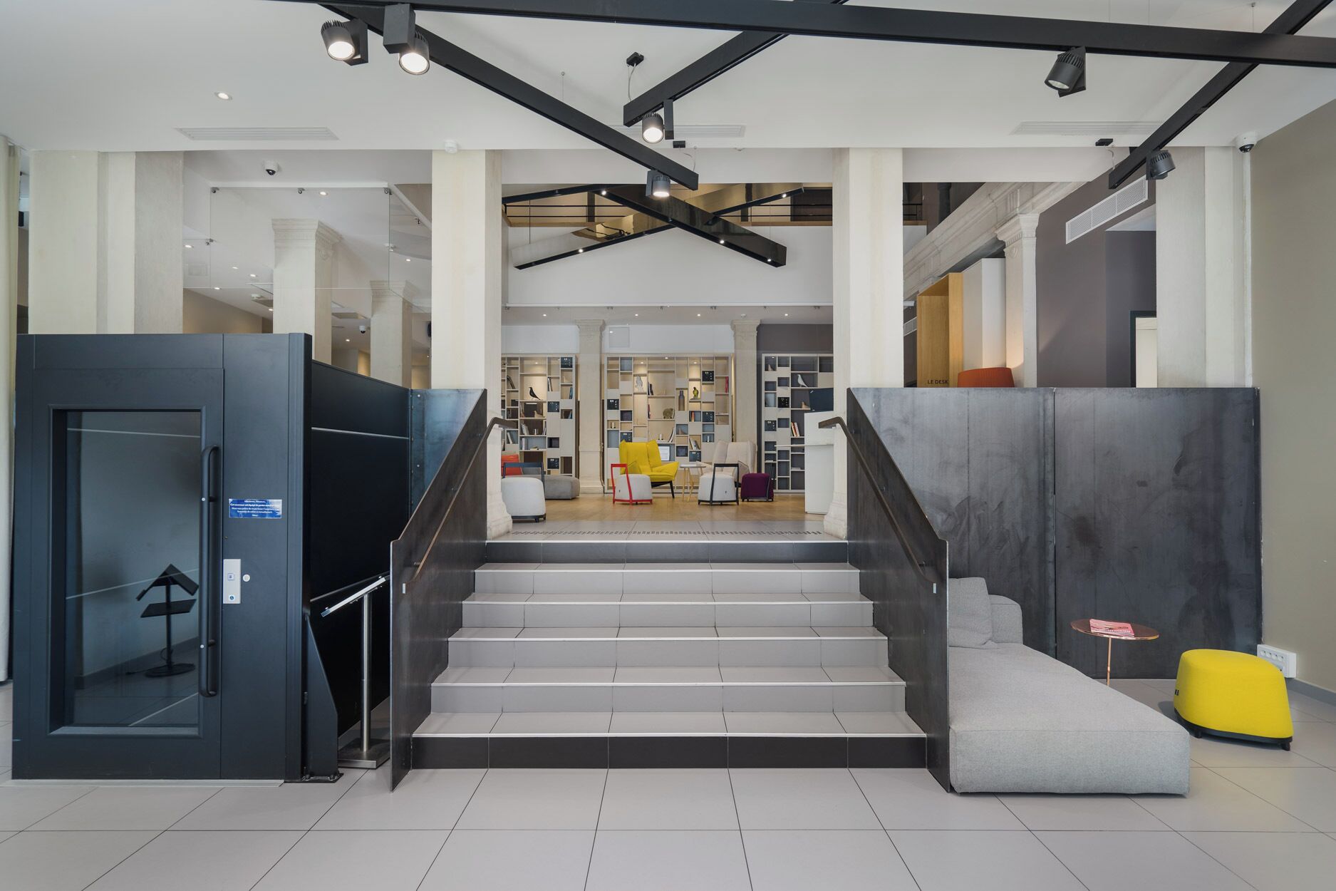 A modern interior with a staircase leading to a seating area with bookshelves.