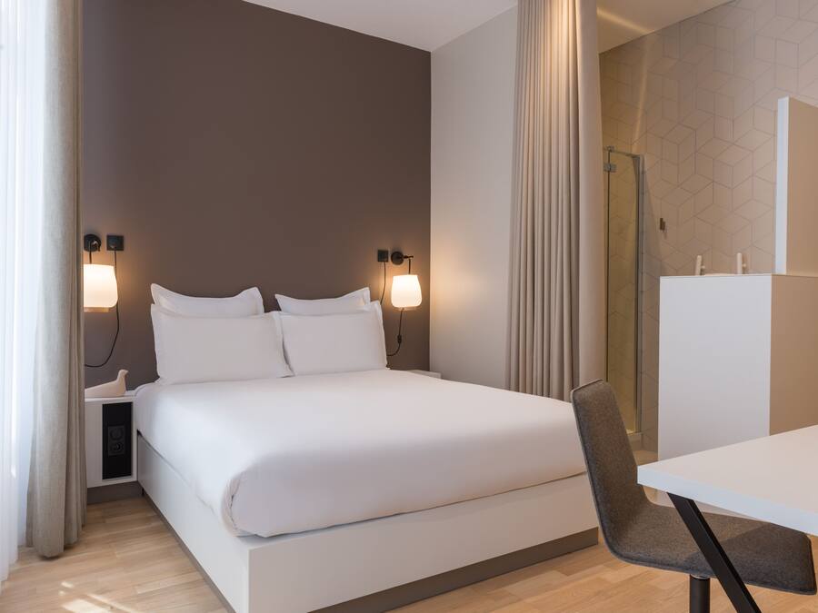 Una habitación de hotel moderna con una cama grande, lámparas de noche, un escritorio y una silla.