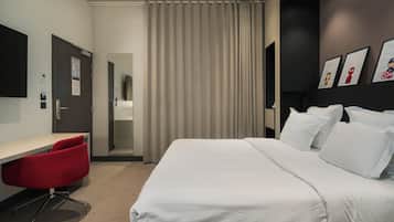 A hotel room with a bed, a desk, a red chair, a mirror, and a curtain.