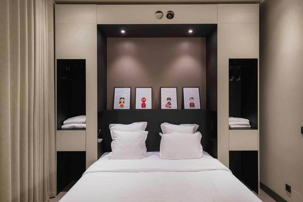 A modern hotel room with a large bed, two bedside tables, and a headboard with framed artwork.