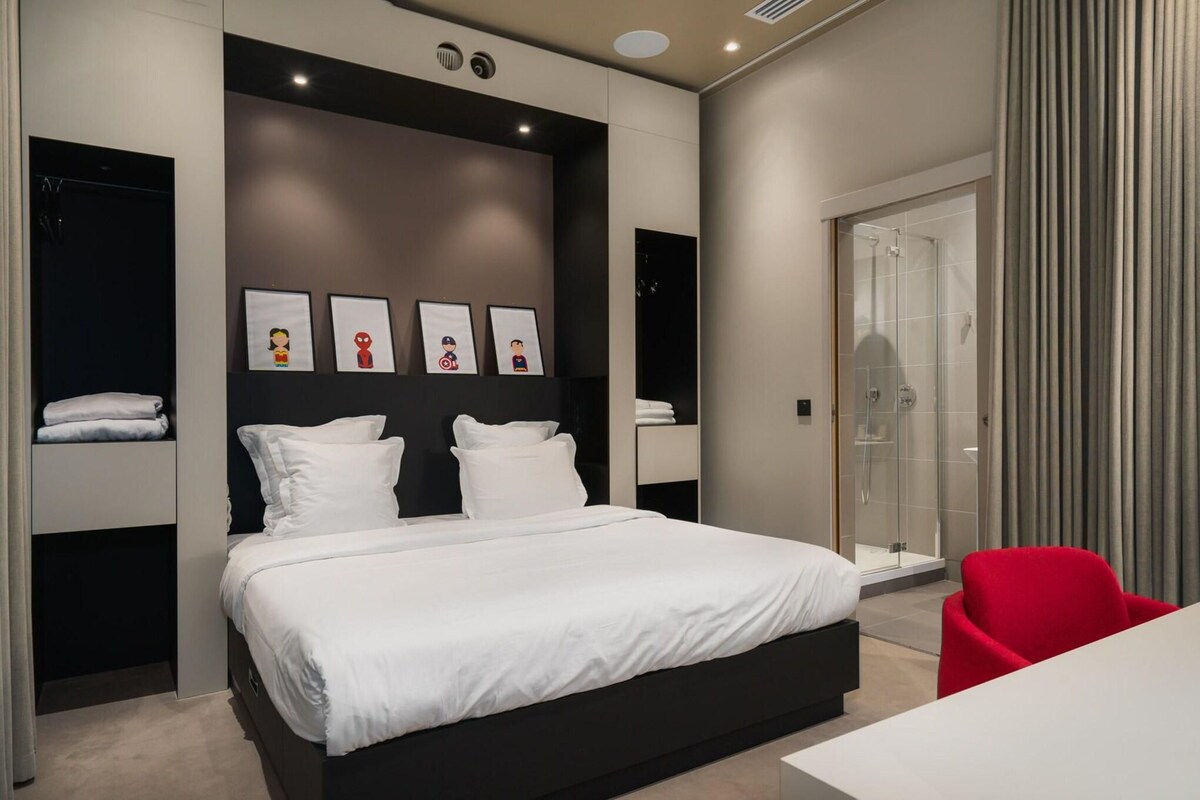 A modern bedroom with a large bed, a red chair, a glass shower, and framed pictures on the wall.