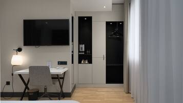 A modern hotel room with a desk, chair, flat-screen TV, wardrobe, and a bed.
