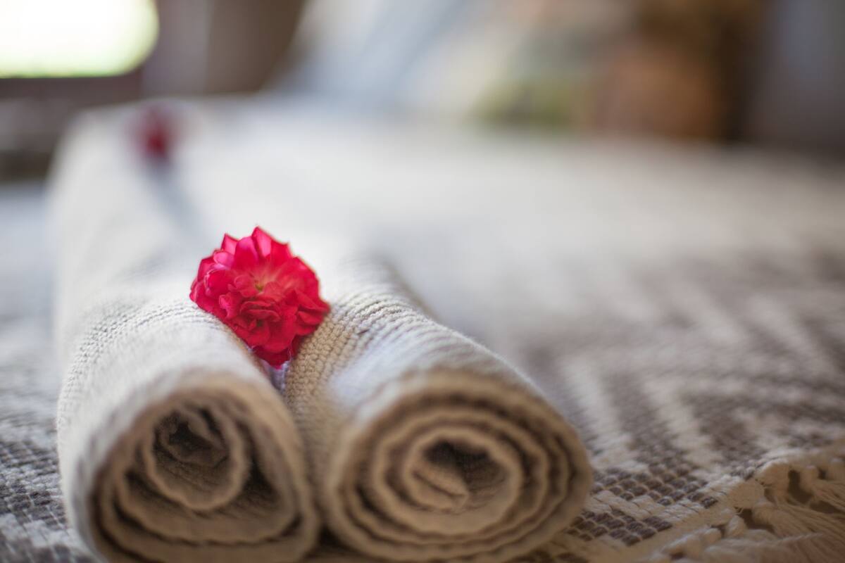 Een netjes opgerolde handdoek met een rode bloem op een gestructureerd oppervlak.