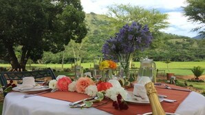 Una mesa para comer al aire libre con manteles blancos, centros de mesa florales y una botella de champán.