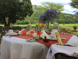 Una mesa para comer al aire libre con manteles blancos, centros de mesa florales y una botella de champán.