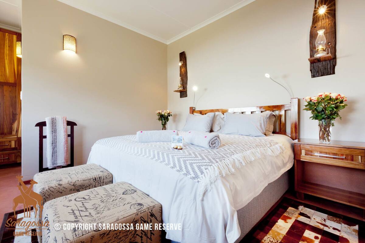 Een keurig opgemaakt slaapkamer met een groot bed, nachtkastjes, een houten nachtkastje en een bankje.
