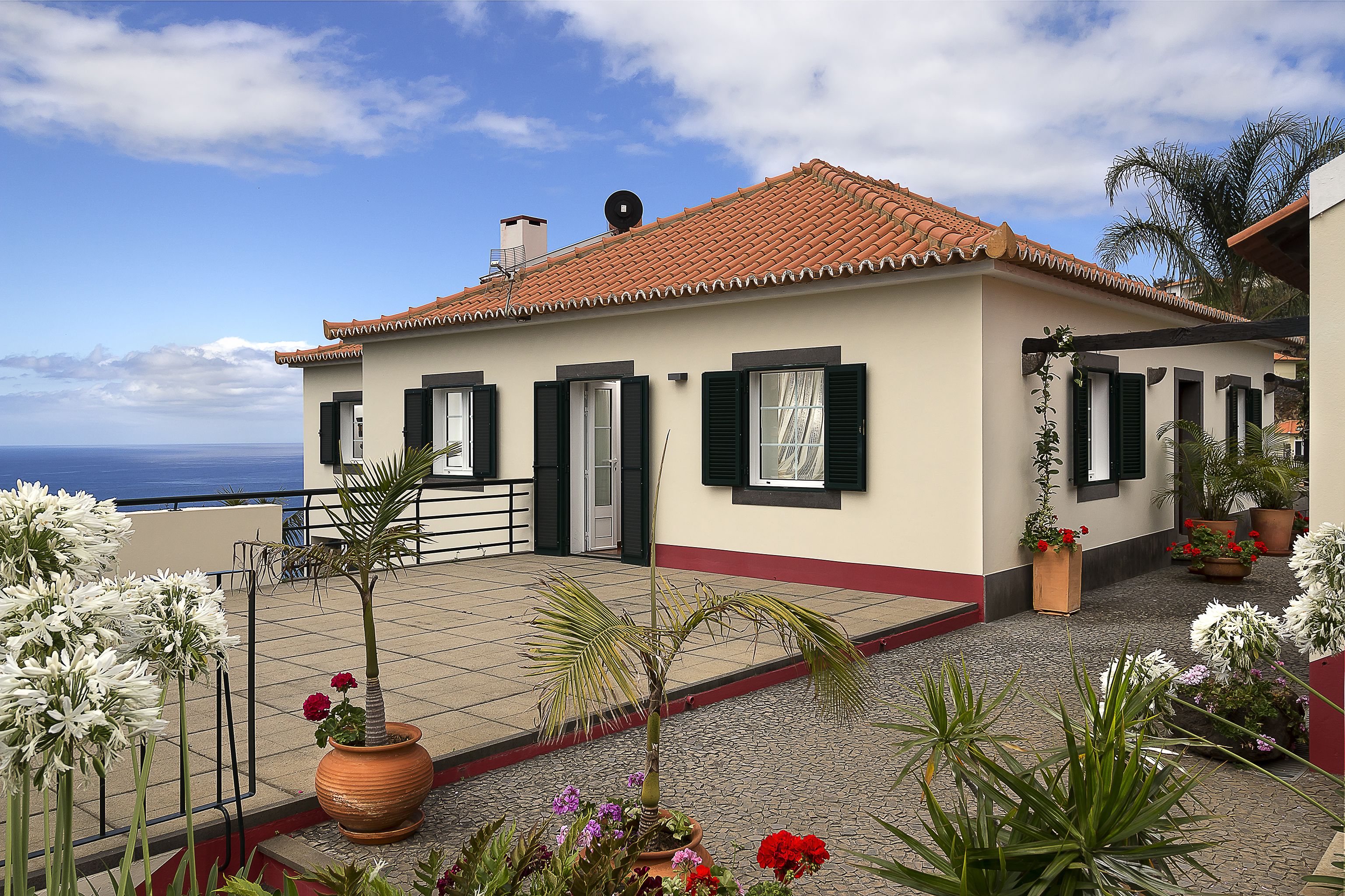 A two-story building with a tiled roof, a balcony with potted plants, and a view of the sea.