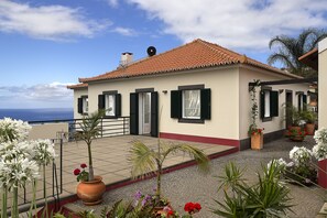Ein zweistöckiges Gebäude mit einem Ziegeldach, einem Balkon mit Blumentöpfen und Blick auf das Meer.