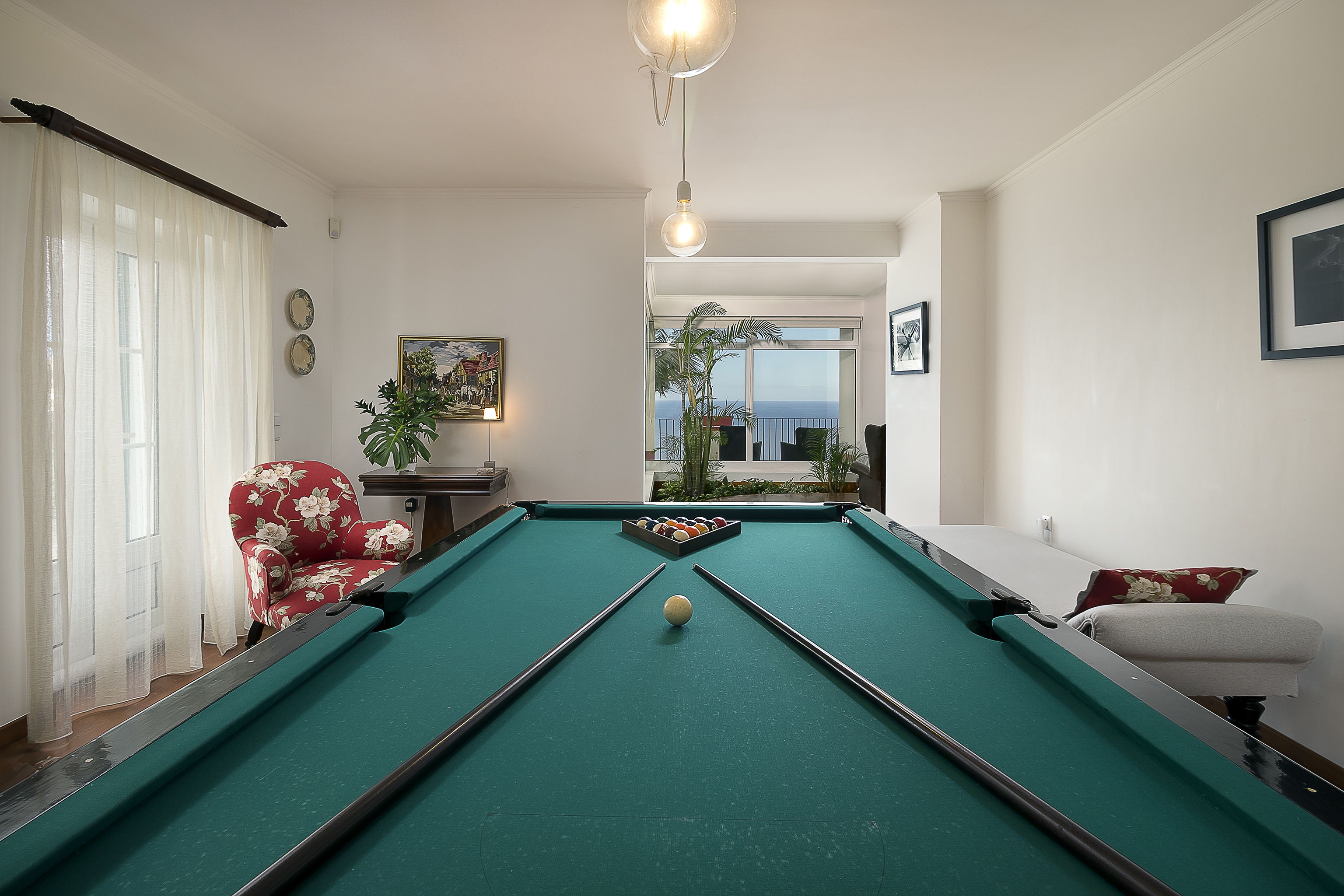 A pool table with balls, a floral armchair, and a view of the outdoors.