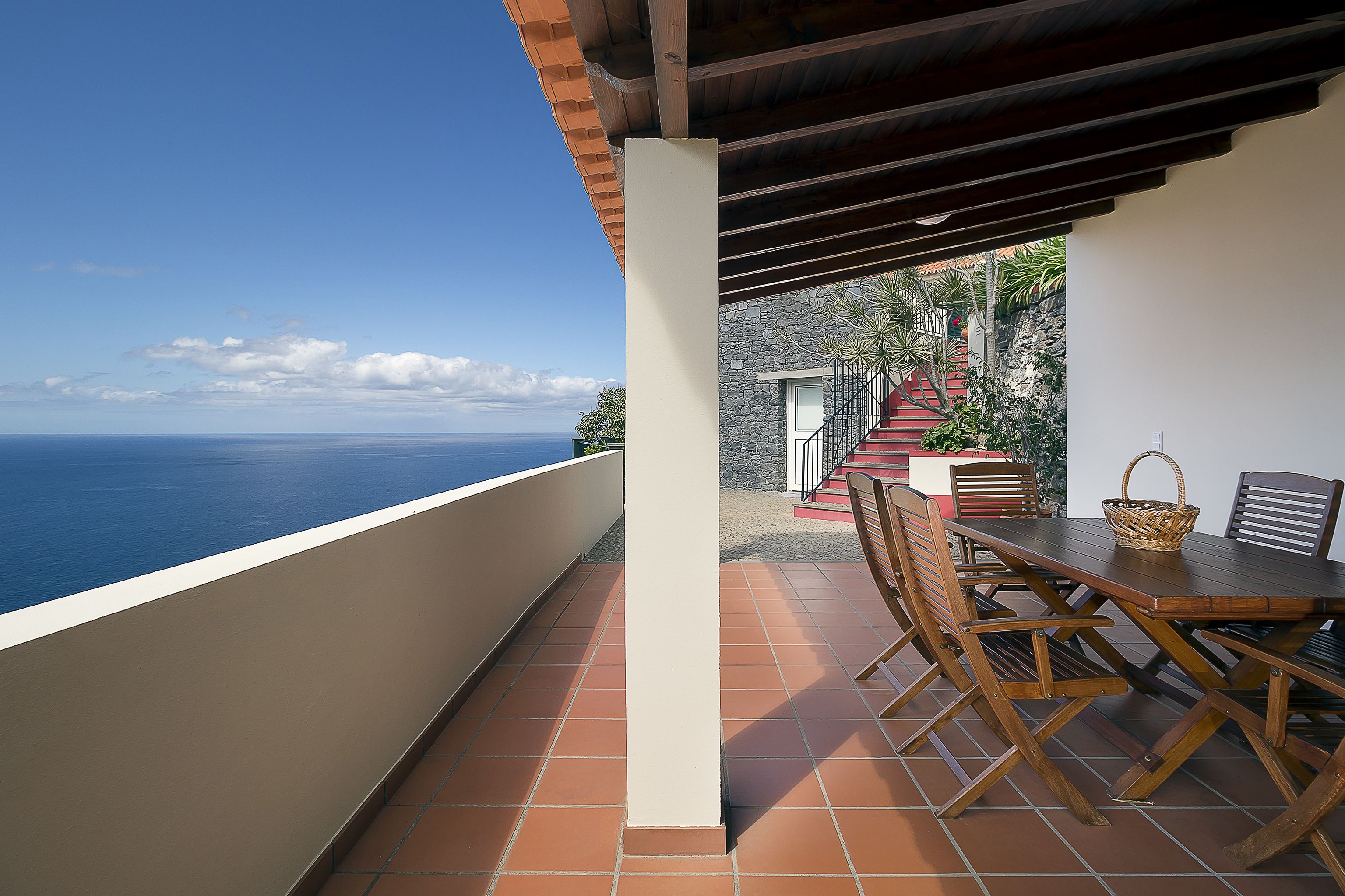 Un balcon avec vue sur la mer, une table en bois avec des chaises et un mur en pierre.