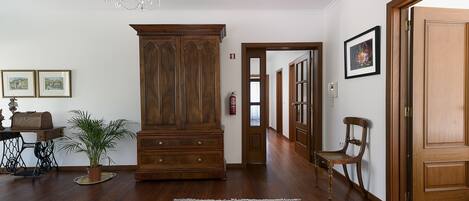 Ein geräumiger Raum mit Holzböden, einem großen Schrank aus Holz, einer Kristallleuchtreibe und einem roten Teppich mit Muster.