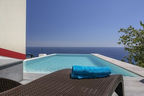 A pool with a blue towel on a lounge chair, overlooking a clear blue sky and the sea. - Casa do Julio by Our Madeira (Calheta)