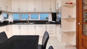 Una cocina con armarios blancos, encimera negra y vistas al mar a través de las ventanas.