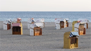 Strandhütten mit gestreiften Markisen und nummerierten Schildern, die auf einem sandigen Strand mit Blick auf das Meer angeordnet sind.