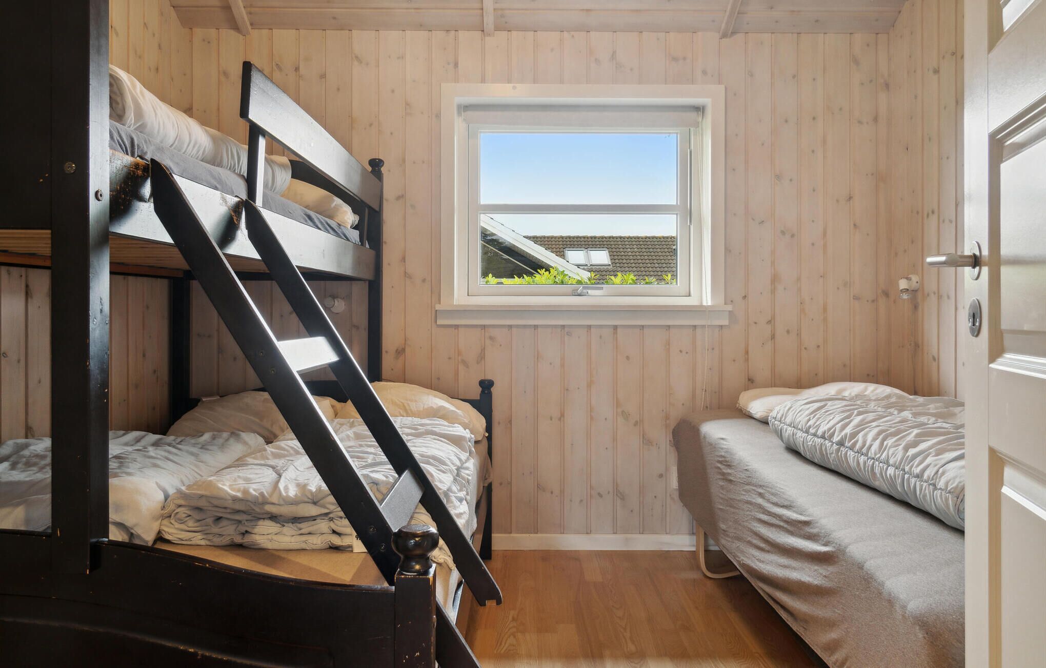A small, wooden-paneled room with two bunk beds and a window providing a view of the outside.