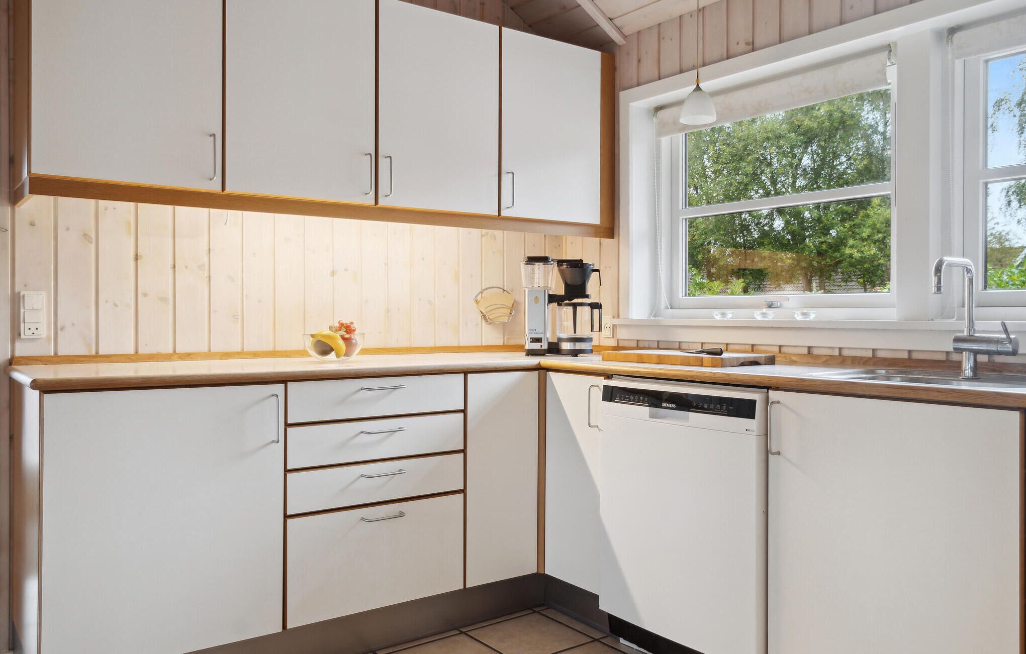 A kitchen with white cabinets, a window with a view of trees, a coffee maker, and a dishwasher.