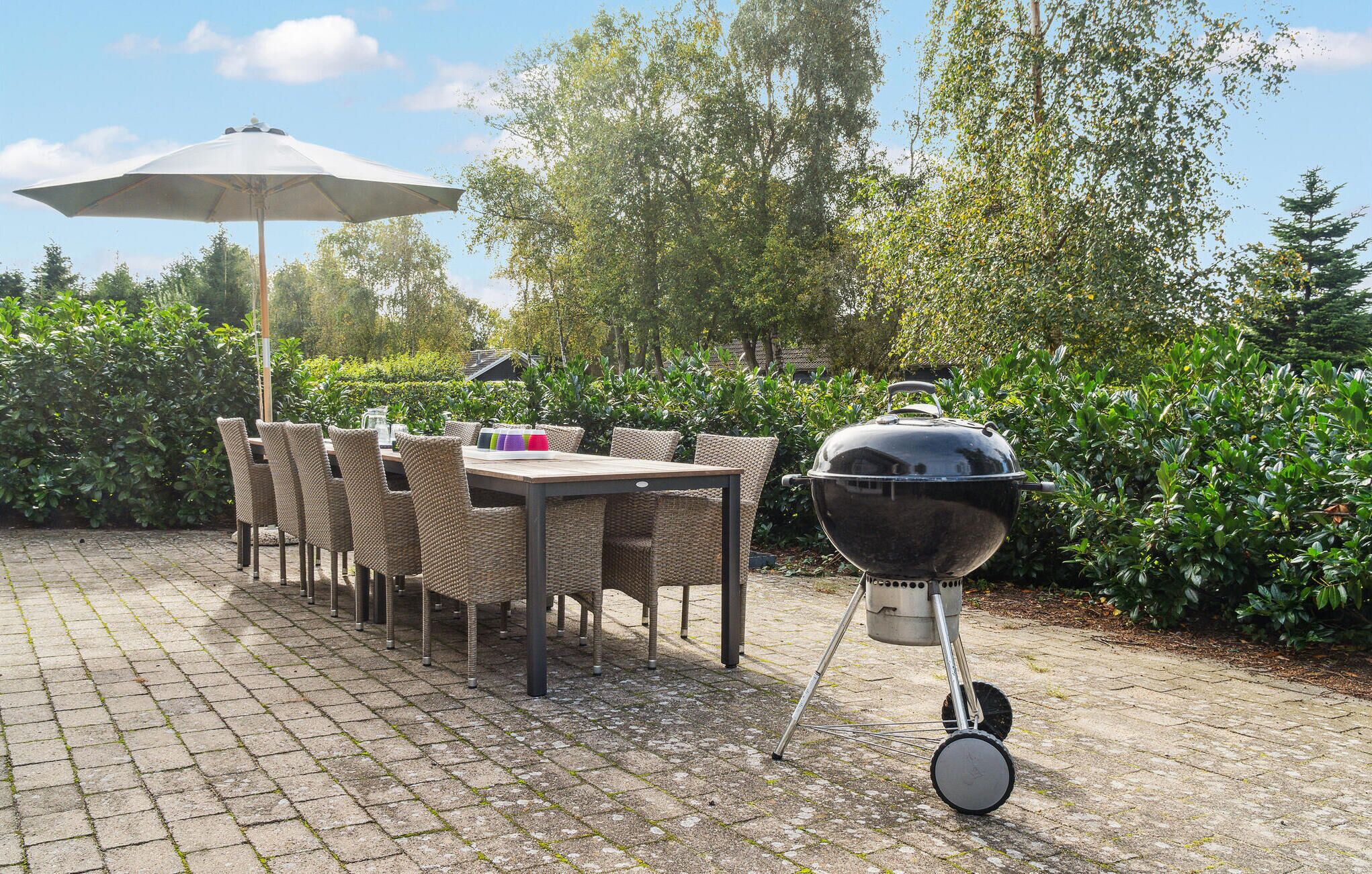 Une terrasse extérieure avec une table et des chaises, un barbecue et un grand parasol.