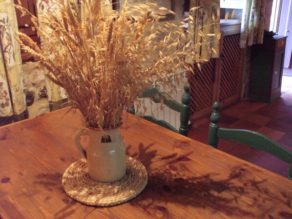 Una mesa de madera con un camino tejido y un jarrón de trigo seco.