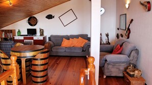 A cozy living room with a gray sofa, wooden coffee table, and a dining table with stools. There is a kitchen area with a refrigerator and a sink. - Casa Jardim Mar by Our Madeira (Calheta)