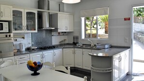 A modern kitchen with white cabinets, a granite countertop, and a dining area with a white table and chairs. - Casa Jardim Mar by Our Madeira (Calheta)