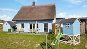 A house with a thatched roof, a patio with chairs, and a small playhouse. - Nice home in Glowe with WiFi (Glowe)