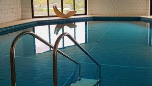 Une piscine intérieure aux carreaux bleu clair, un élément décoratif en bois au-dessus de la piscine et des échelles métalliques pour y accéder.