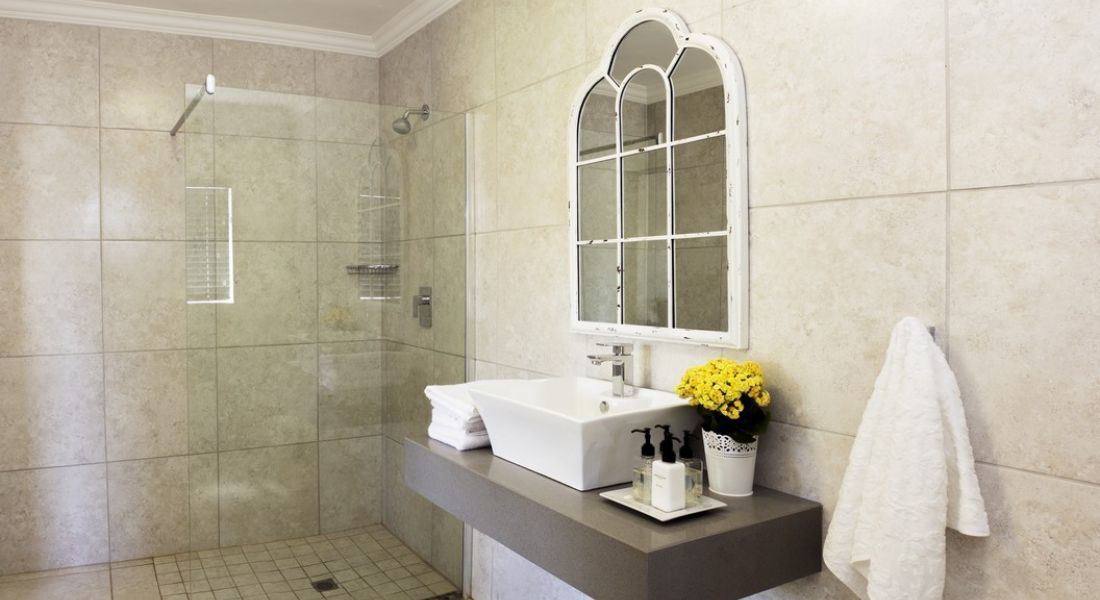 Un baño moderno con ducha de vidrio, lavabo blanco y espejo sobre él.