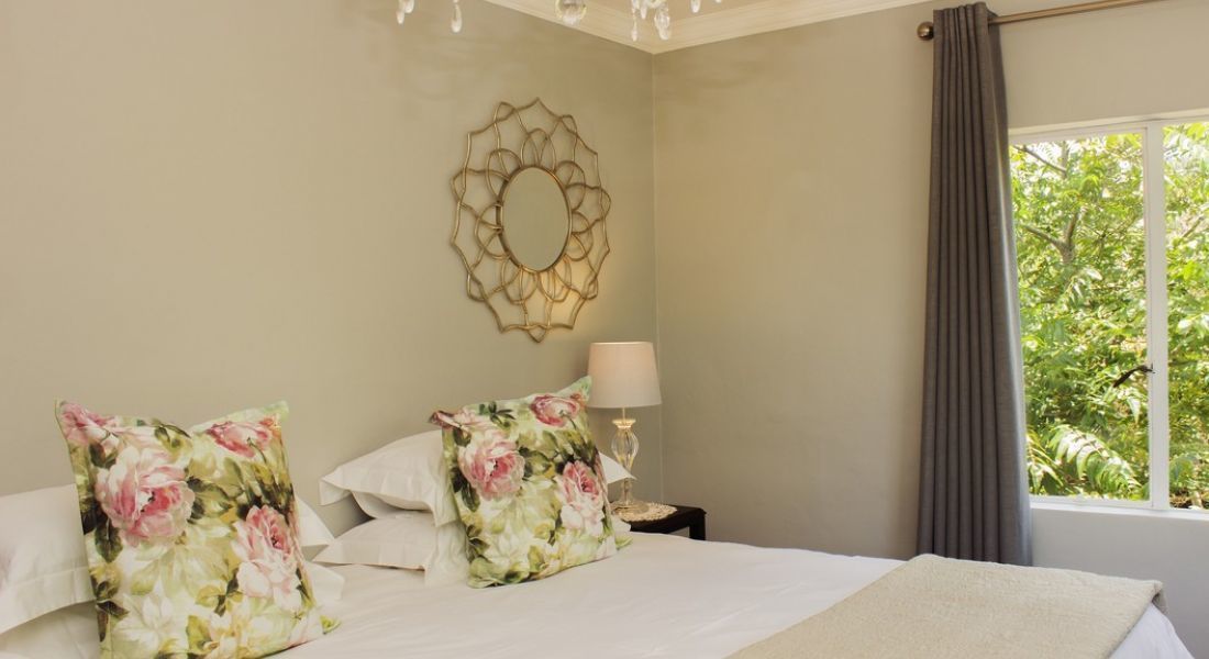 Un dormitorio con cama, almohadones florales, una lámpara de noche y un adorno en la pared.