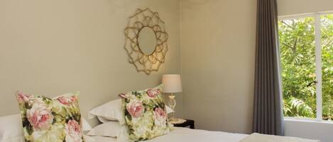 Un dormitorio con cama, almohadones florales, una lámpara de noche y un adorno en la pared.
