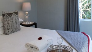 Cama bem arrumada com uma toalha branca enrolada, um travesseiro decorativo, dois copos e uma bandeja com uma tigela estampada.