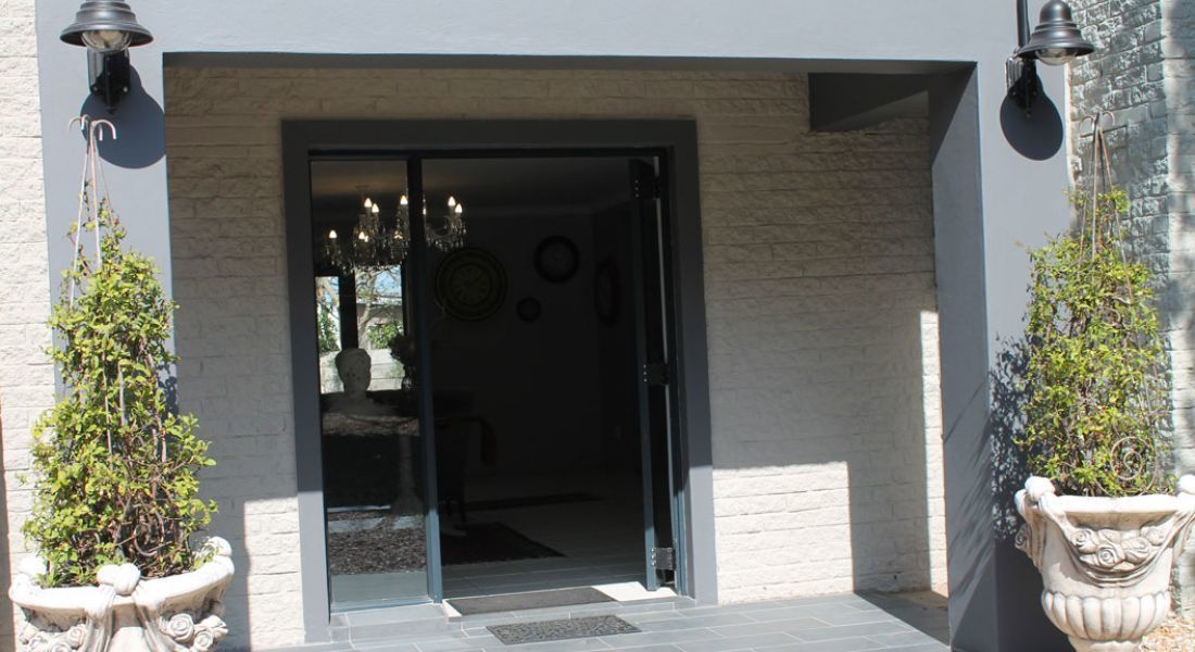 A modern building entrance with a glass door, potted plants, and a chandelier visible inside.