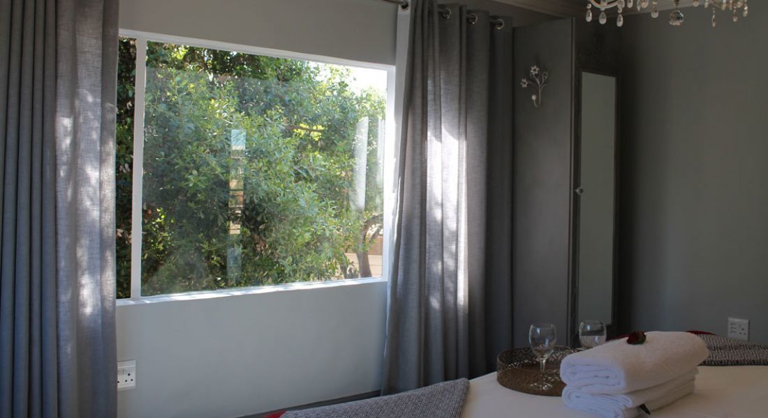 A bedroom with a large window, a bed with white linens, a bedside table with glasses, and a chandelier.