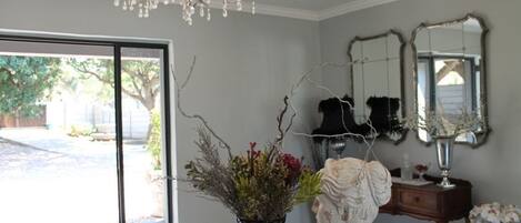 A room with a large window, a chandelier, a vase with flowers, and a mirror on the wall.